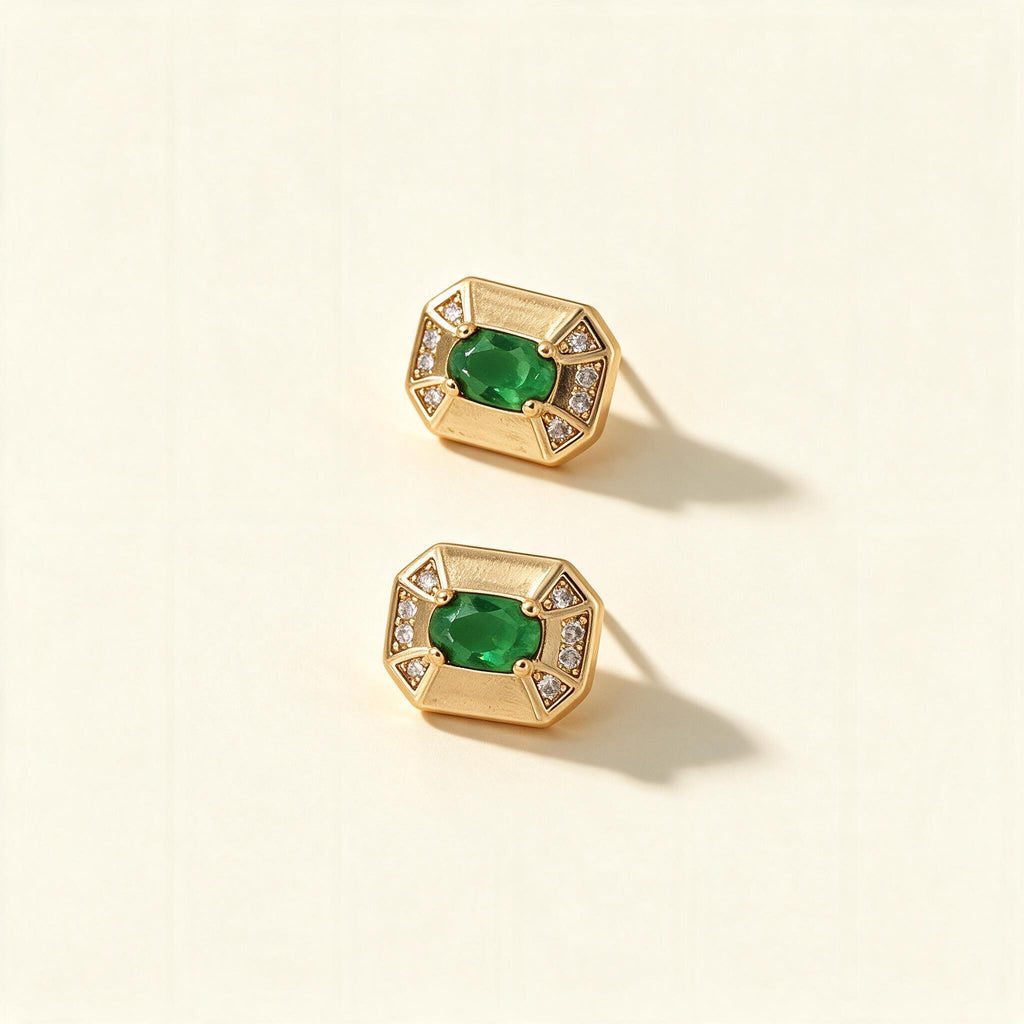 Gold-tone octagonal stud earrings with emerald green oval stone and cubic zirconia corners on ivory background