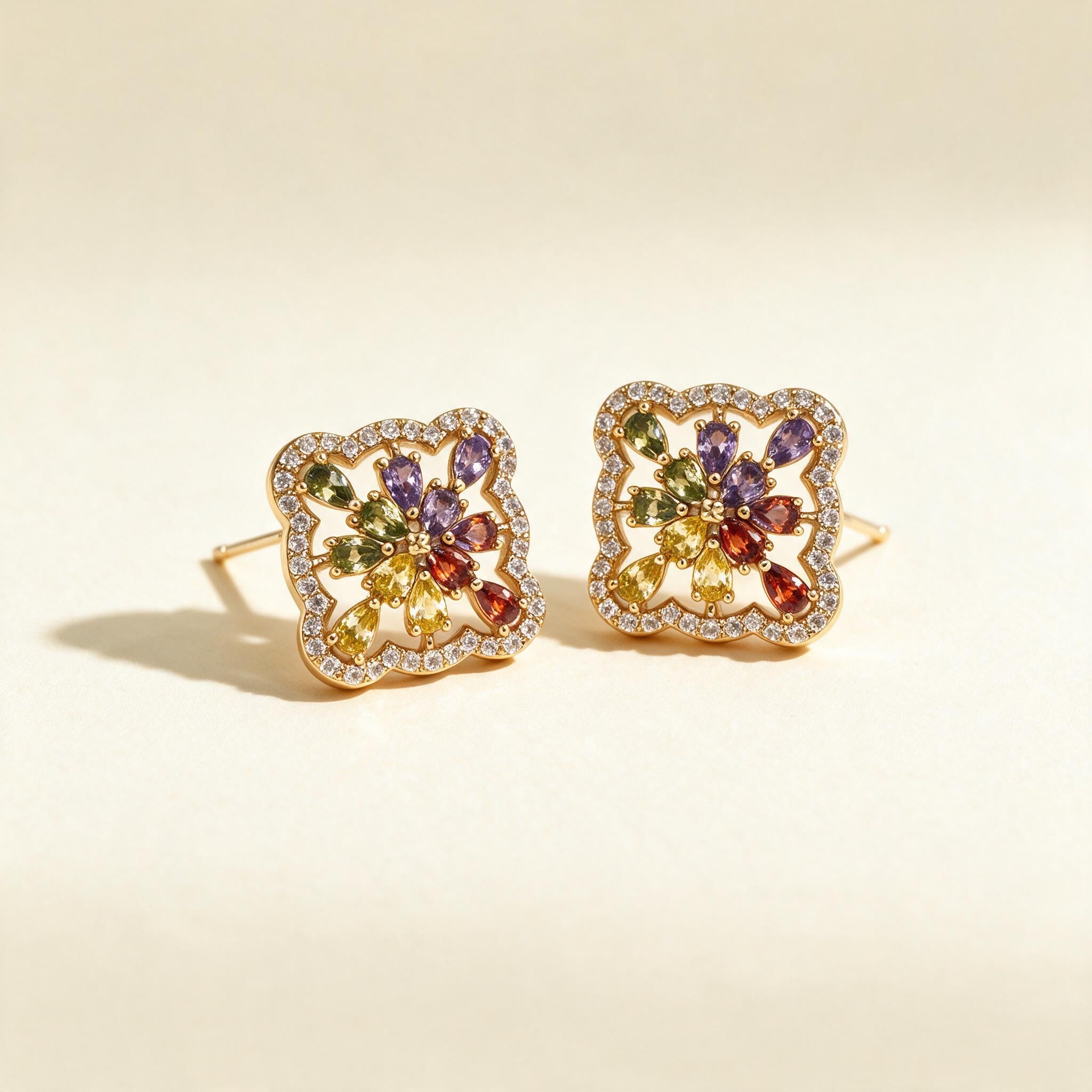 Gold-tone square stud earrings with purple, green, yellow and red pear-cut crystal flower in a pave frame on ivory background