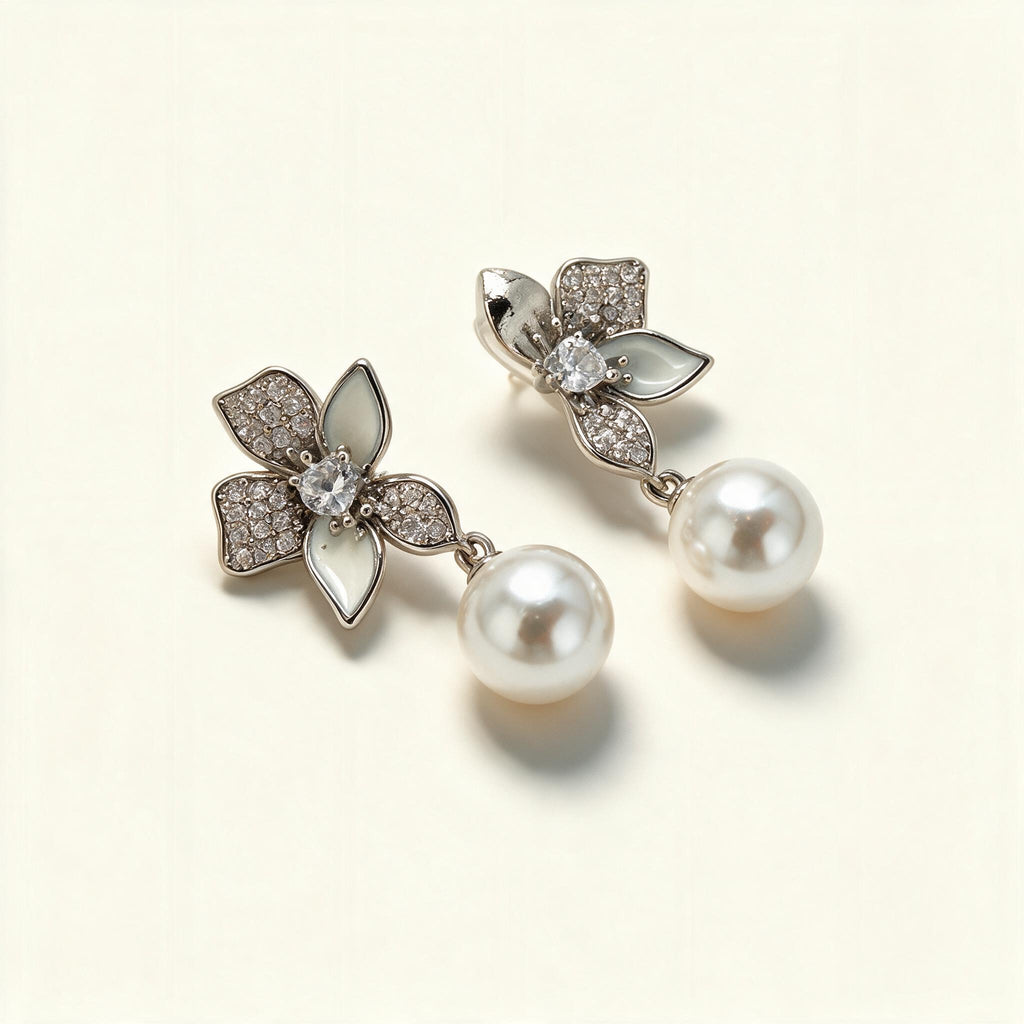 Silver-tone flower earrings with cubic zirconia and white enamel petals and a hanging shell pearl on ivory background
