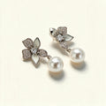 Silver-tone flower earrings with cubic zirconia and white enamel petals and a hanging shell pearl on ivory background