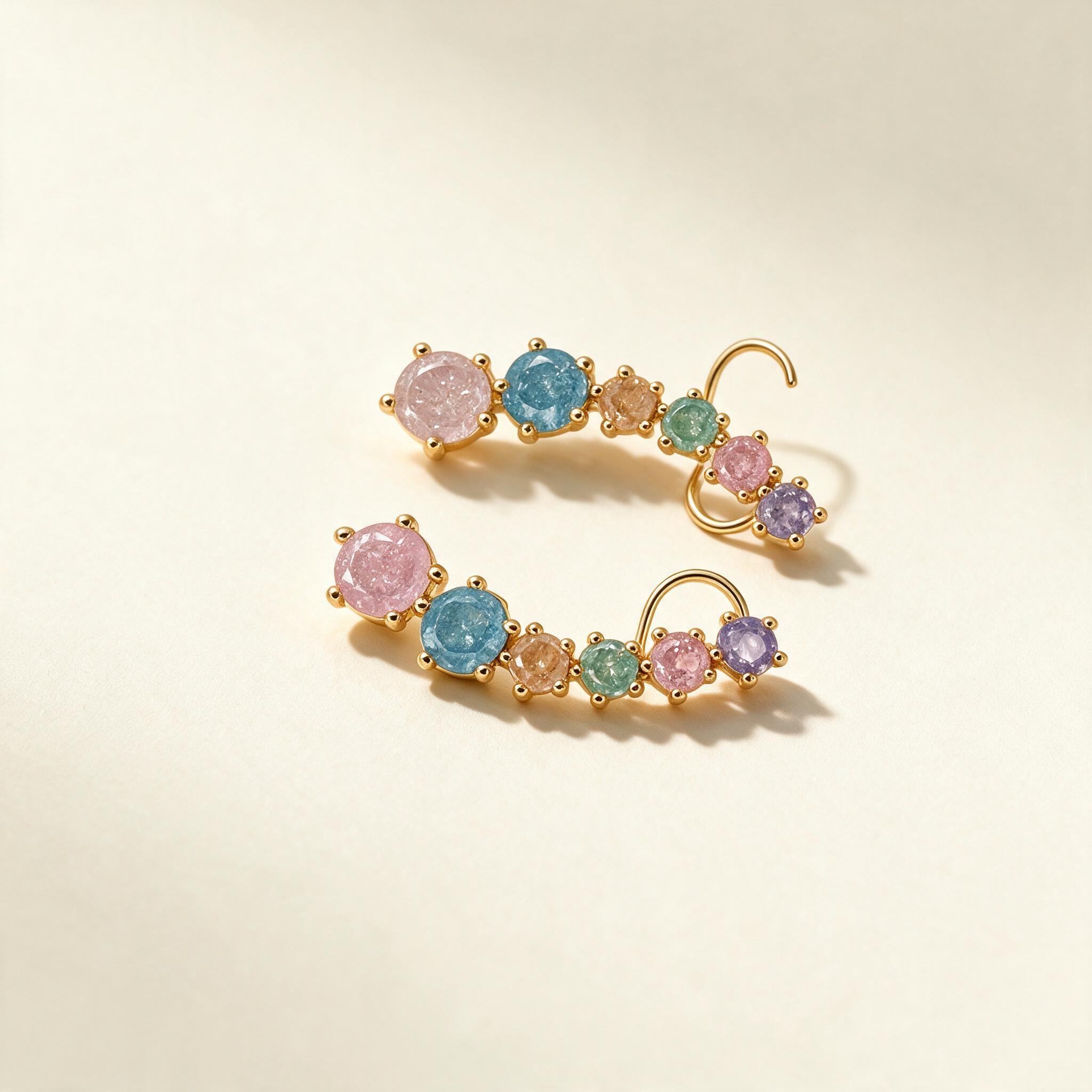 Gold-tone ear climber earrings with six graduated pastel pink, blue, mint and lilac crystals on ivory background