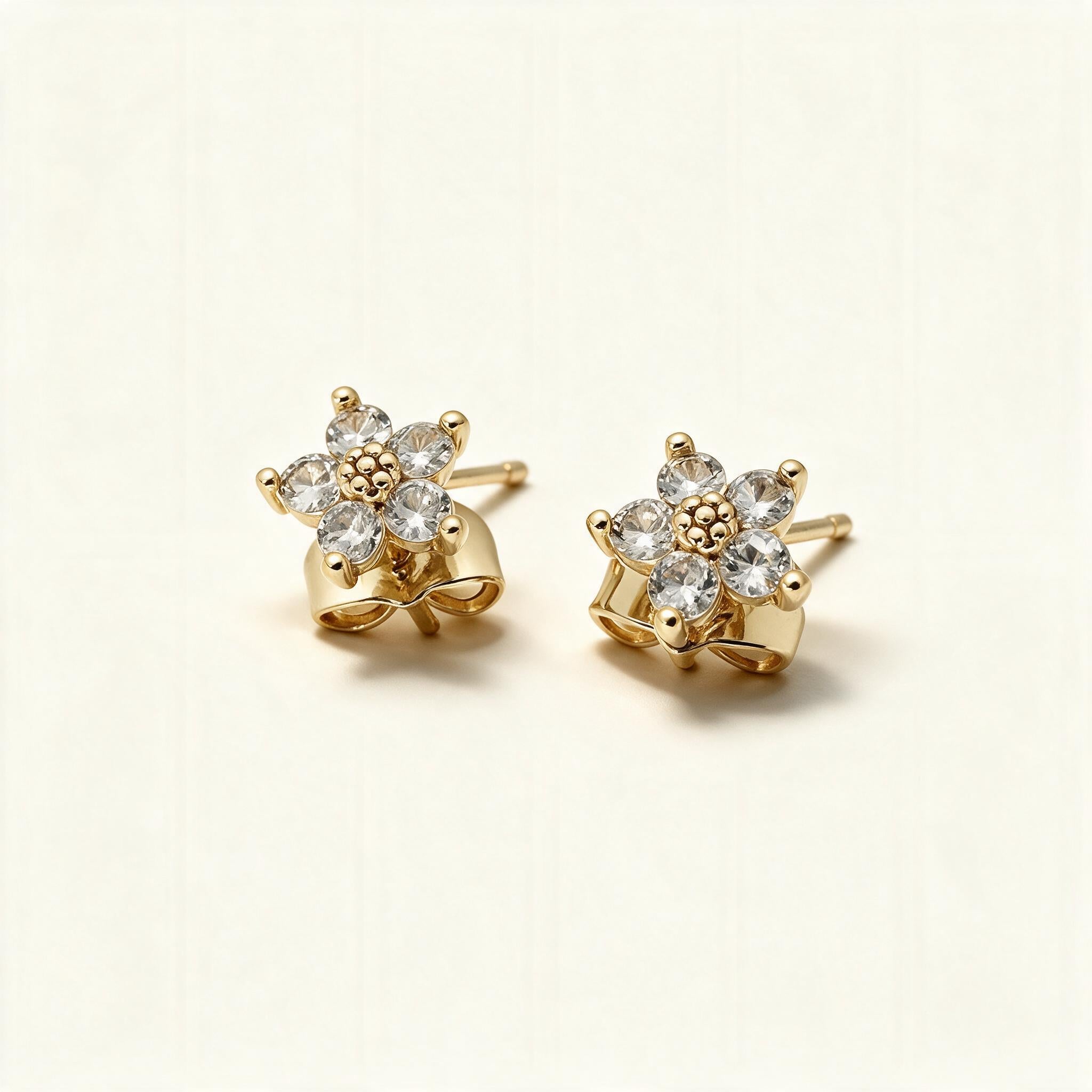 Gold-tone flower stud earrings with five cubic zirconia petals on ivory background