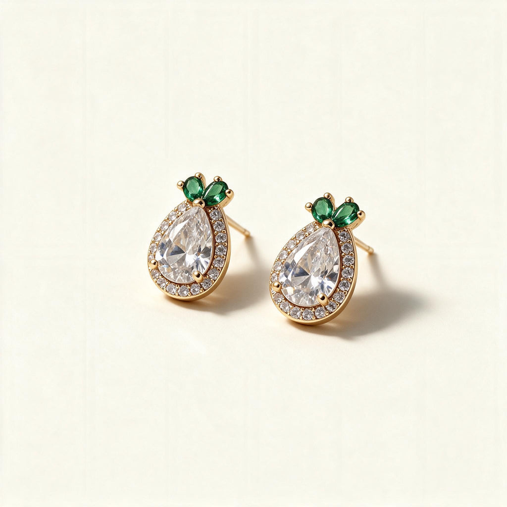 Gold-tone pineapple stud earrings with large pear-cut cubic zirconia halo and emerald green leaf stones on ivory background