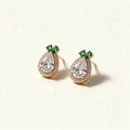 Gold-tone pineapple stud earrings with large pear-cut cubic zirconia halo and emerald green leaf stones on ivory background