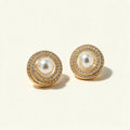 Gold-tone pearl stud earrings with double cubic zirconia halo on ivory background