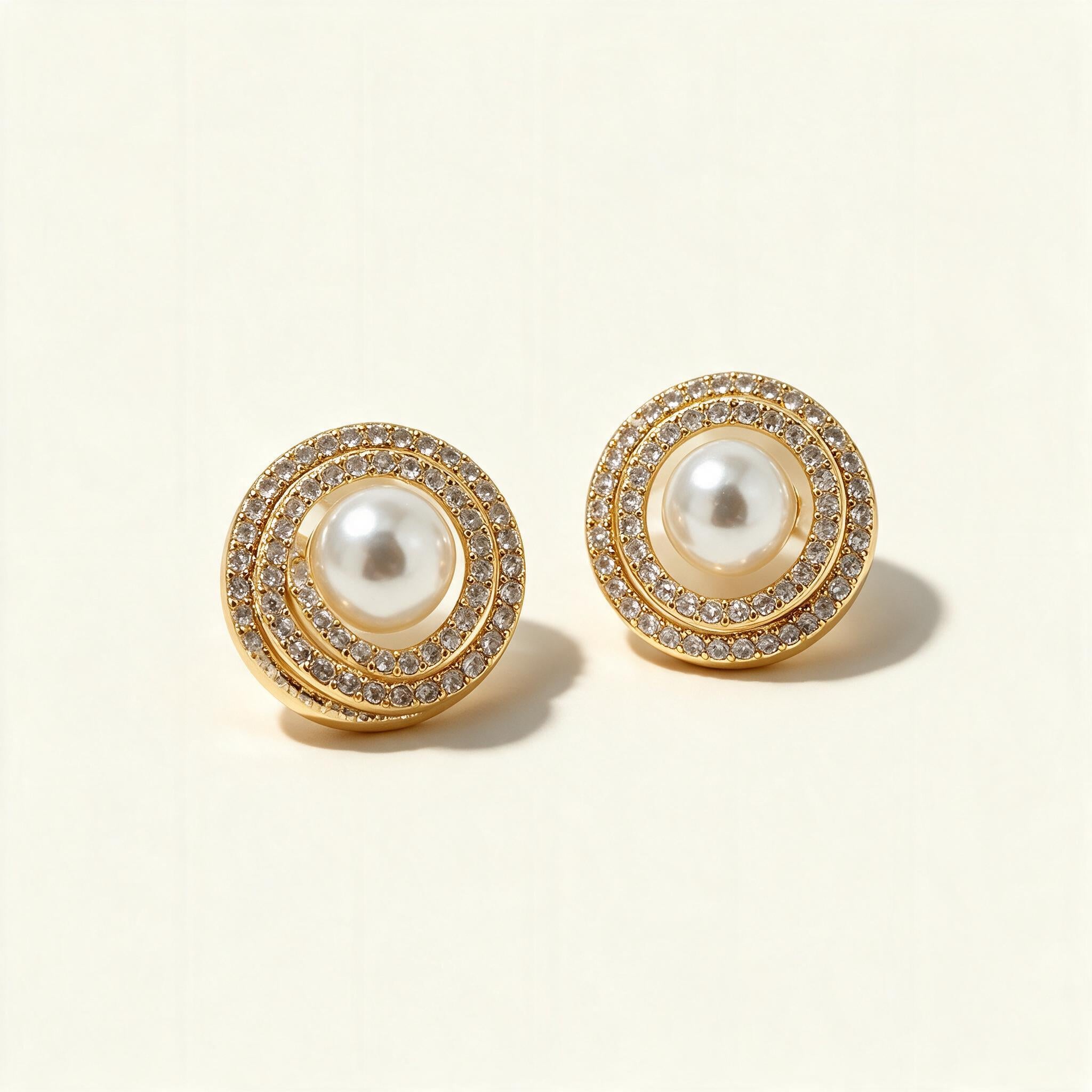 Gold-tone pearl stud earrings with double cubic zirconia halo on ivory background