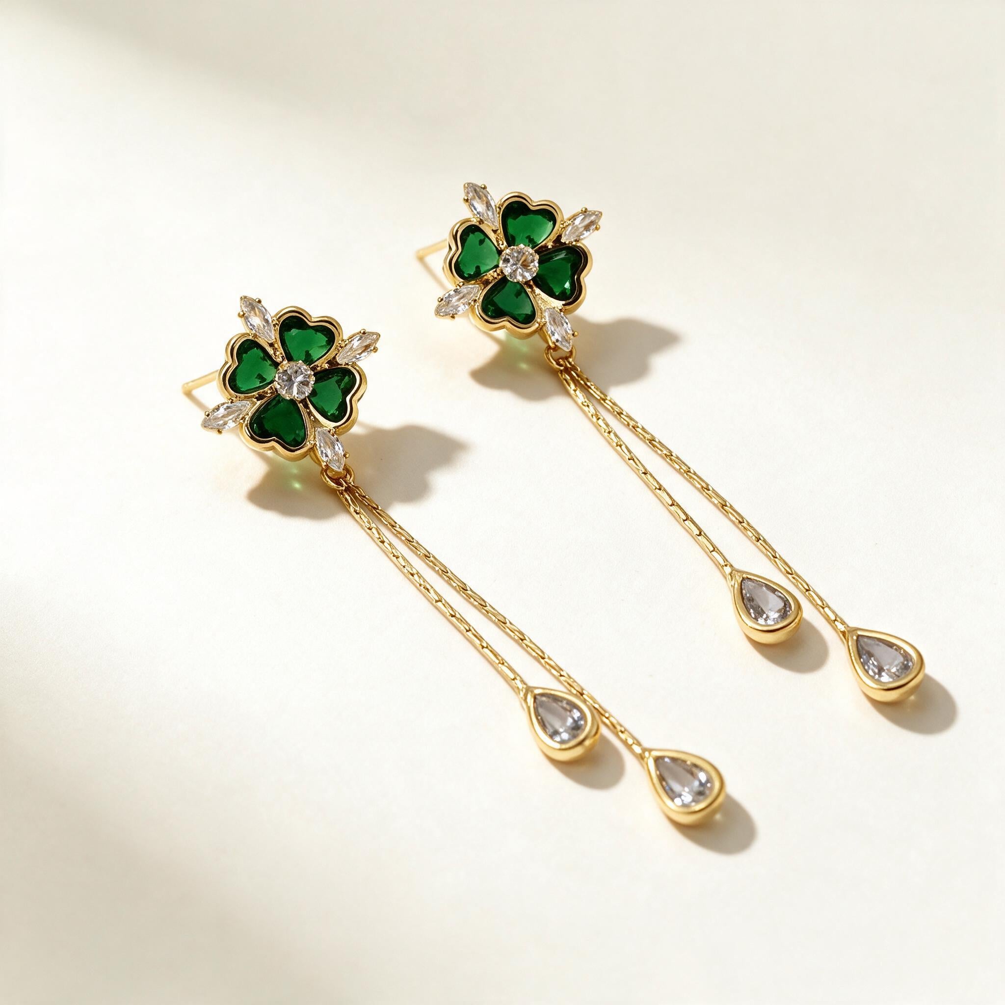 Gold-tone drop earrings with a green heart-petal clover top and two chains ending in clear teardrops