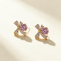 Gold-tone pave bow stud earrings with a large round pink cubic zirconia on ivory background