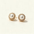 Gold-tone pearl stud earrings with a scalloped sunburst cubic zirconia halo on ivory background