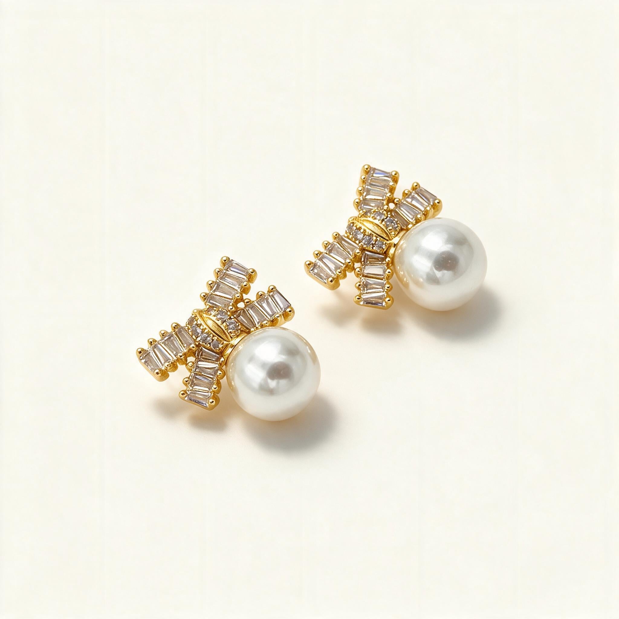 Gold-tone stud earrings with baguette crystal bow motif and large round shell pearl