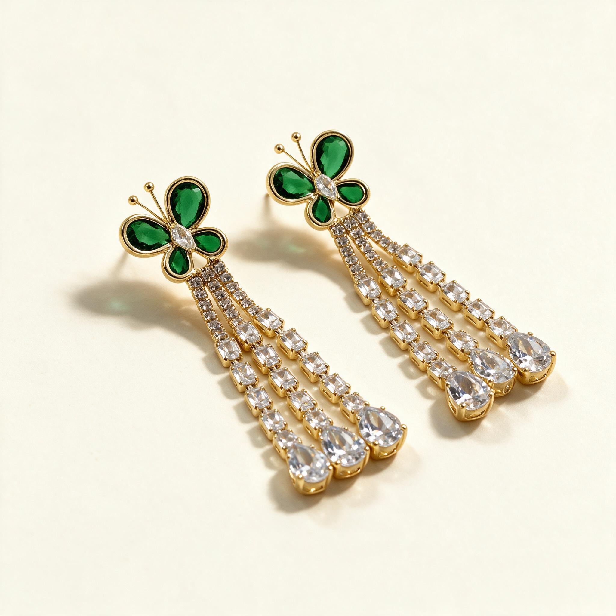 Gold-tone drop earrings with a green stone butterfly top and three crystal strands ending in pear drops