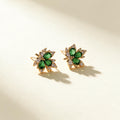 Gold-tone stud earrings with three green pear-cut crystal petals and clear cubic zirconia spray on ivory background