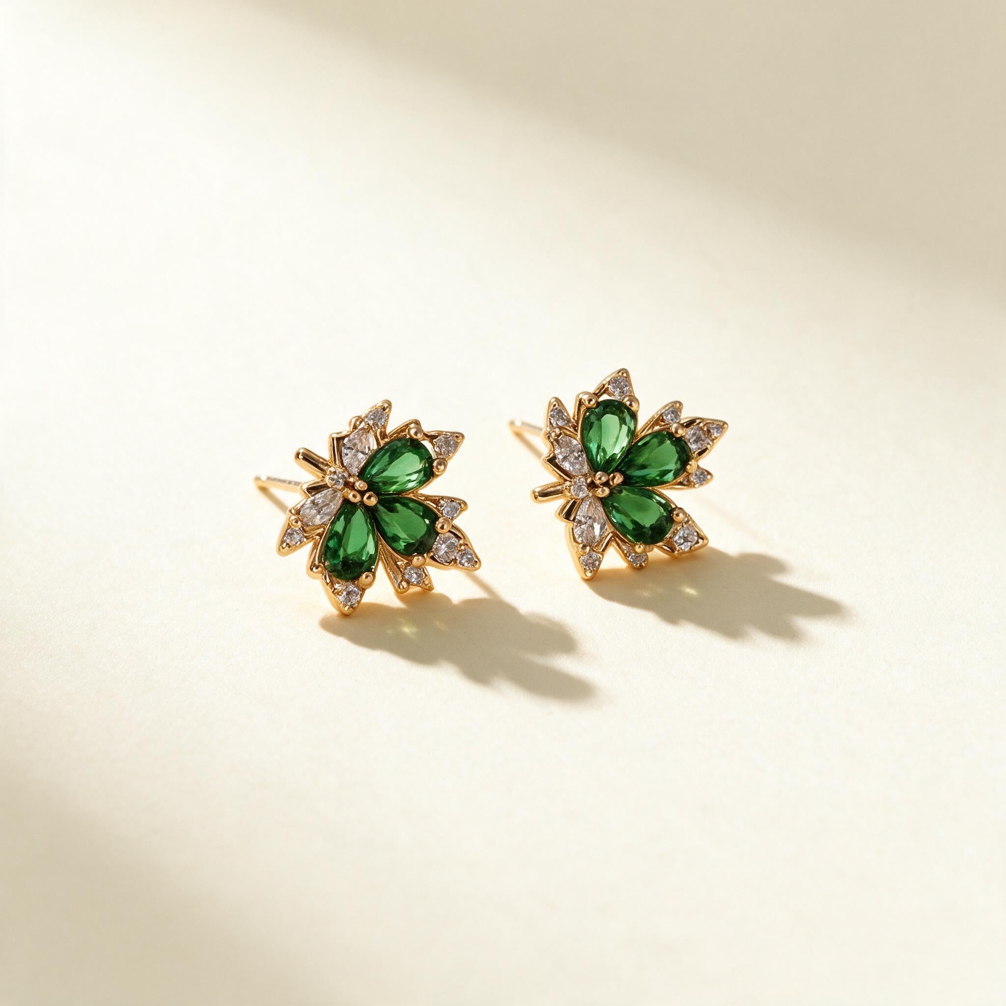 Gold-tone stud earrings with three green pear-cut crystal petals and clear cubic zirconia spray on ivory background