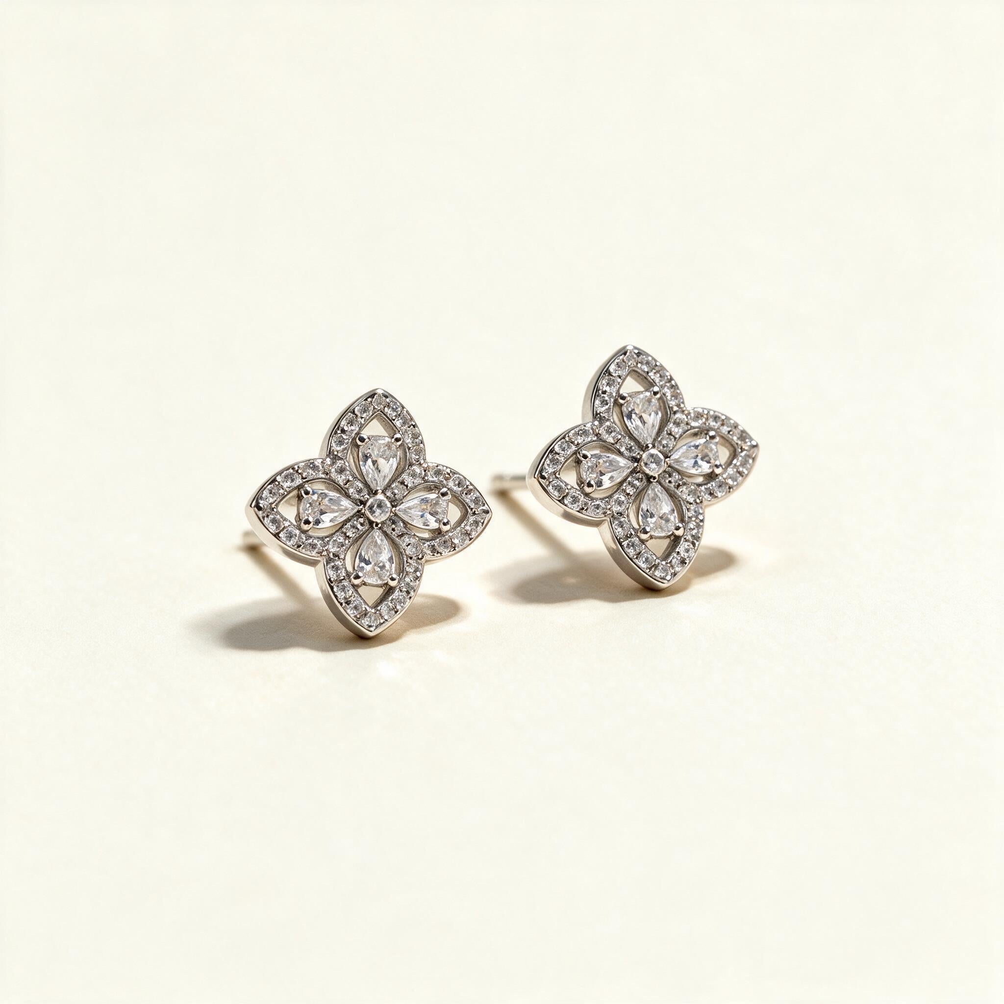 Silver-tone four-petal flower stud earrings outlined in cubic zirconia pave with pear-cut centres on ivory background