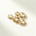 Set of plain polished gold-tone huggie hoop earrings in graduated sizes on ivory background