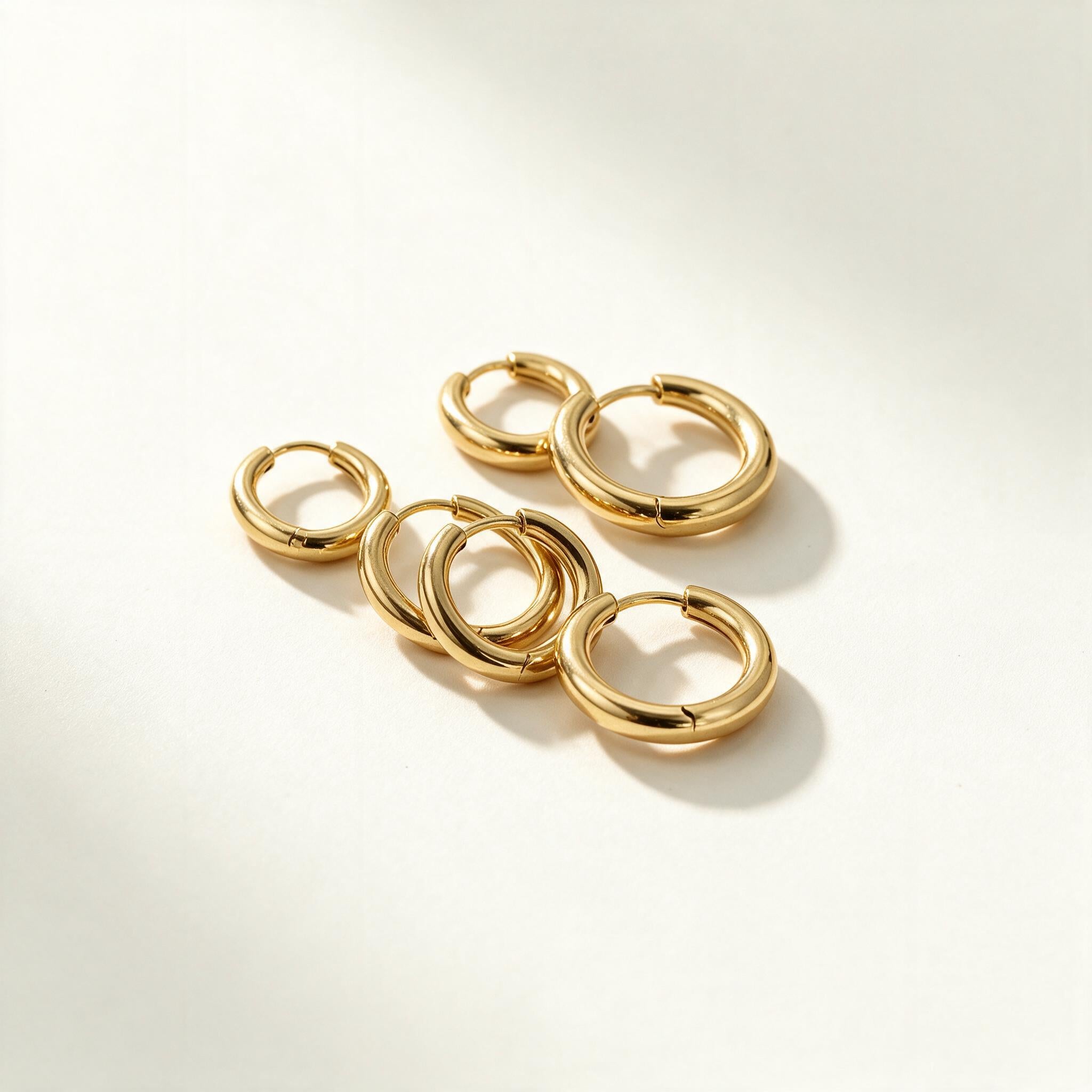 Set of plain polished gold-tone huggie hoop earrings in graduated sizes on ivory background