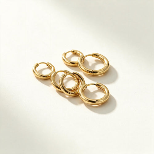 Set of plain polished gold-tone huggie hoop earrings in graduated sizes on ivory background
