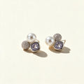 Silver-tone cluster stud earrings with a white shell pearl, cubic zirconia pave bead and lavender cushion-cut crystal on ivory background