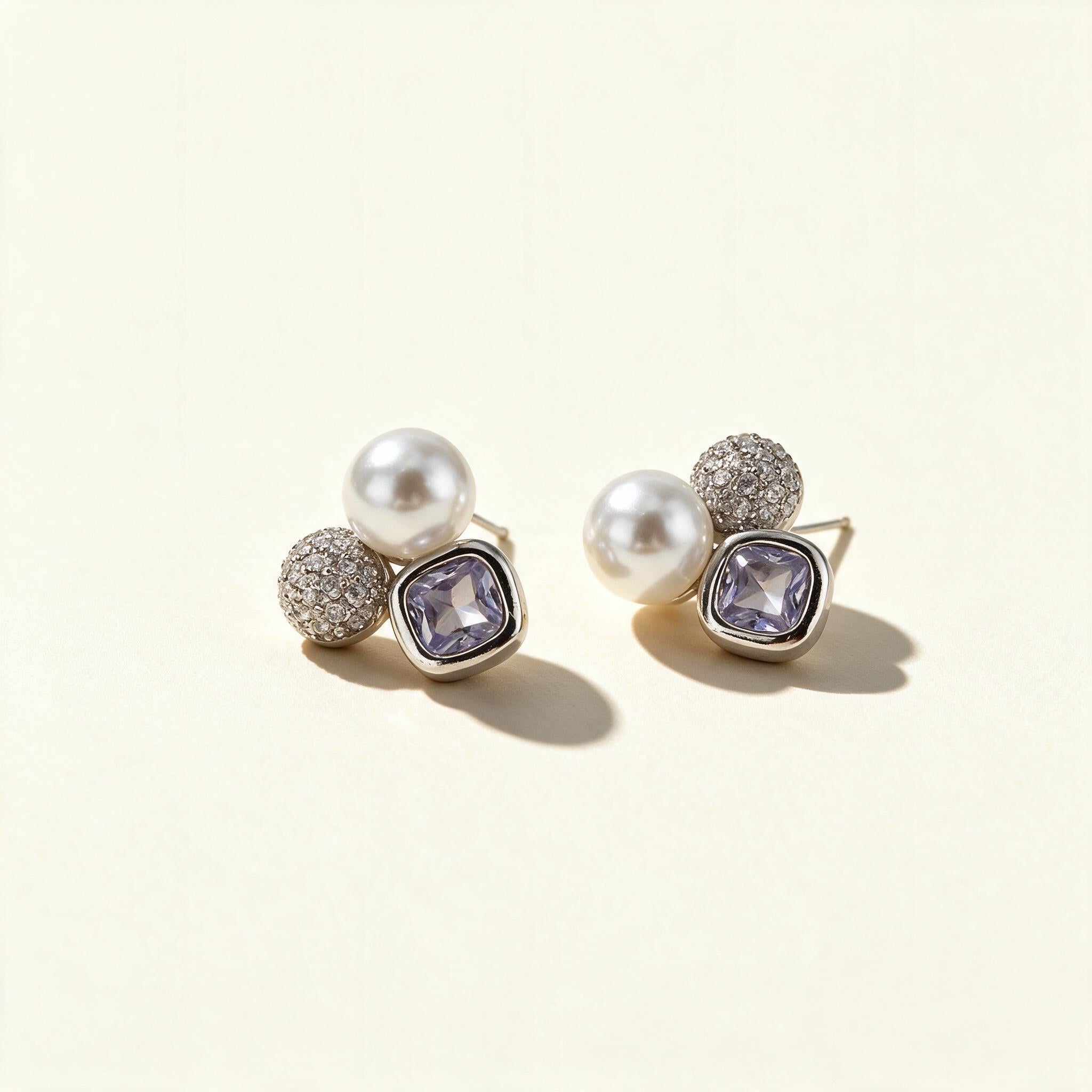 Silver-tone cluster stud earrings with a white shell pearl, cubic zirconia pave bead and lavender cushion-cut crystal on ivory background