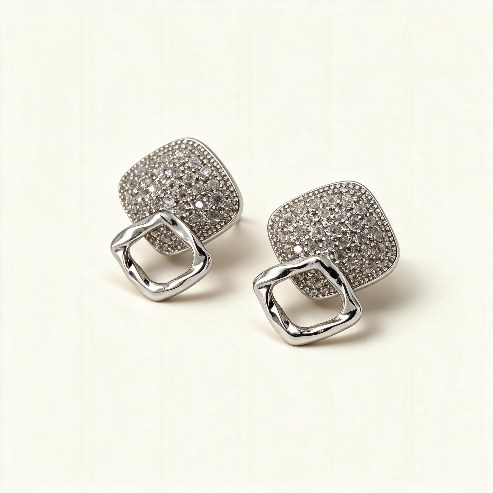 Silver-tone stud earrings with a cubic zirconia pave cushion square and a hammered open square link on ivory background