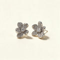 Silver-tone five-petal flower stud earrings paved with cubic zirconia and a round centre stone on ivory background