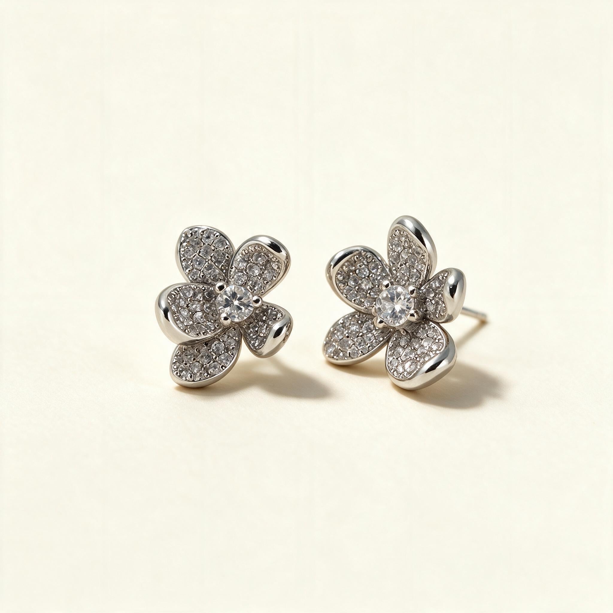 Silver-tone five-petal flower stud earrings paved with cubic zirconia and a round centre stone on ivory background