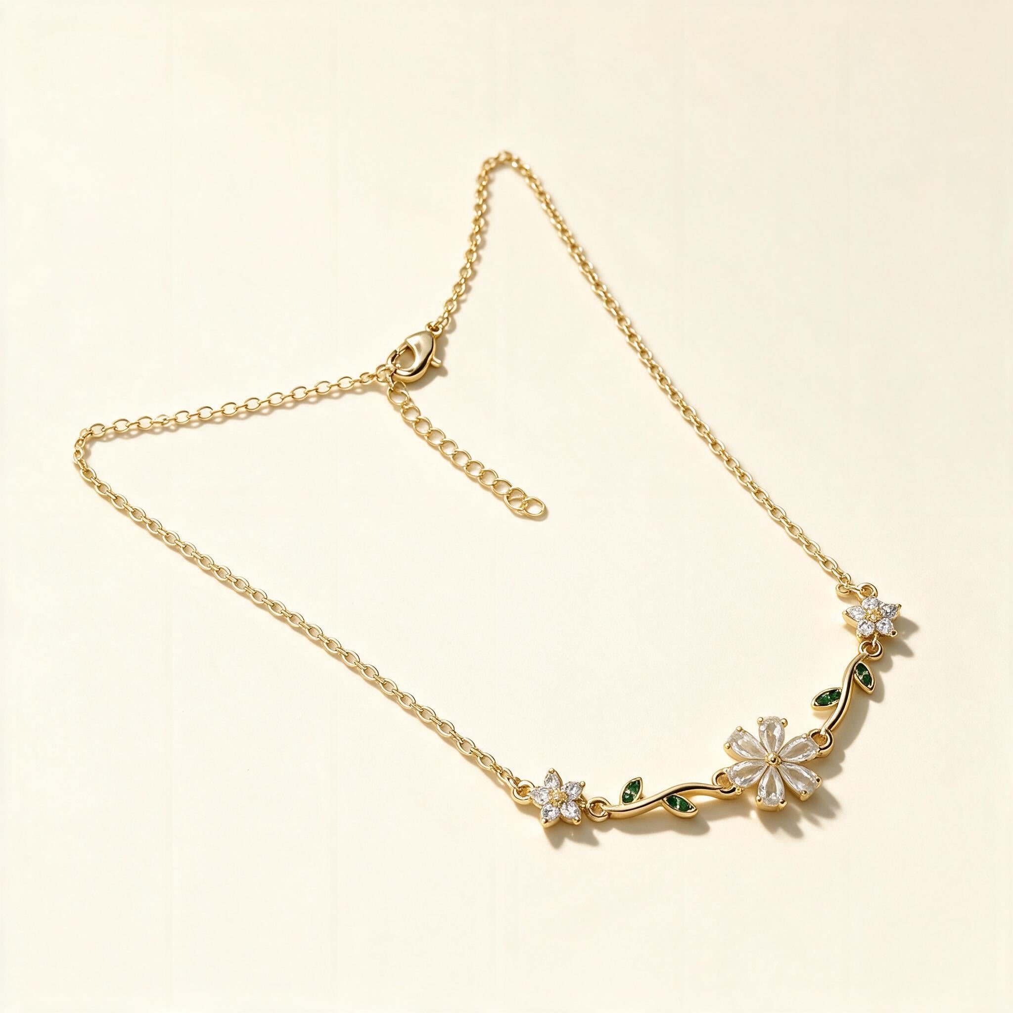 Gold-tone fine chain necklace with crystal flower and green leaf accents