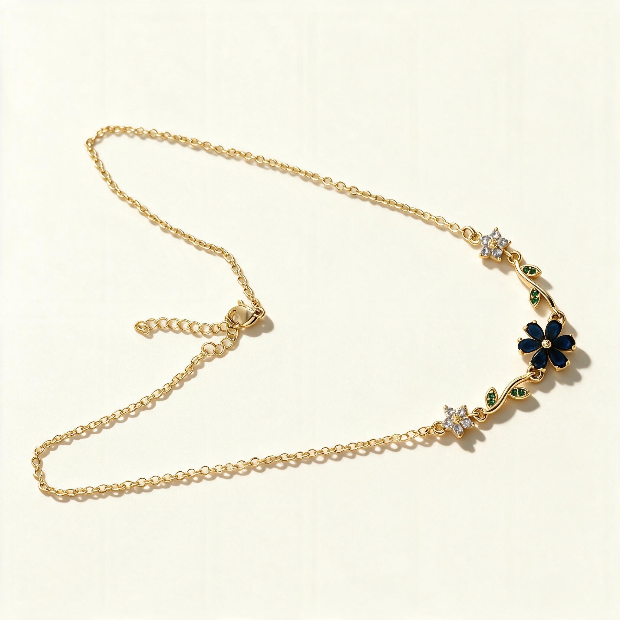Gold-tone chain necklace with navy blue enamel flower and green leaf accents