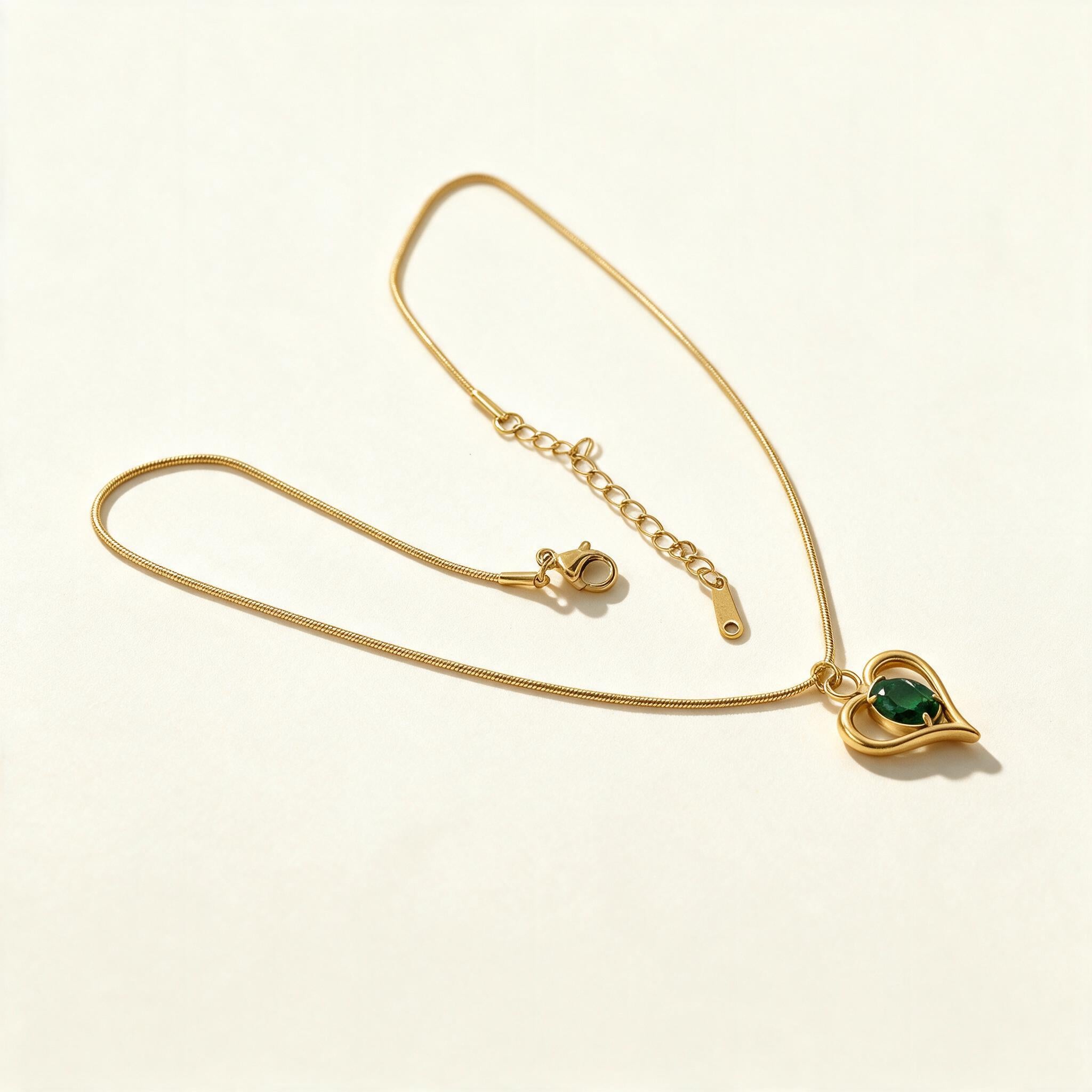Gold-tone snake chain necklace with open heart pendant and green emerald stone