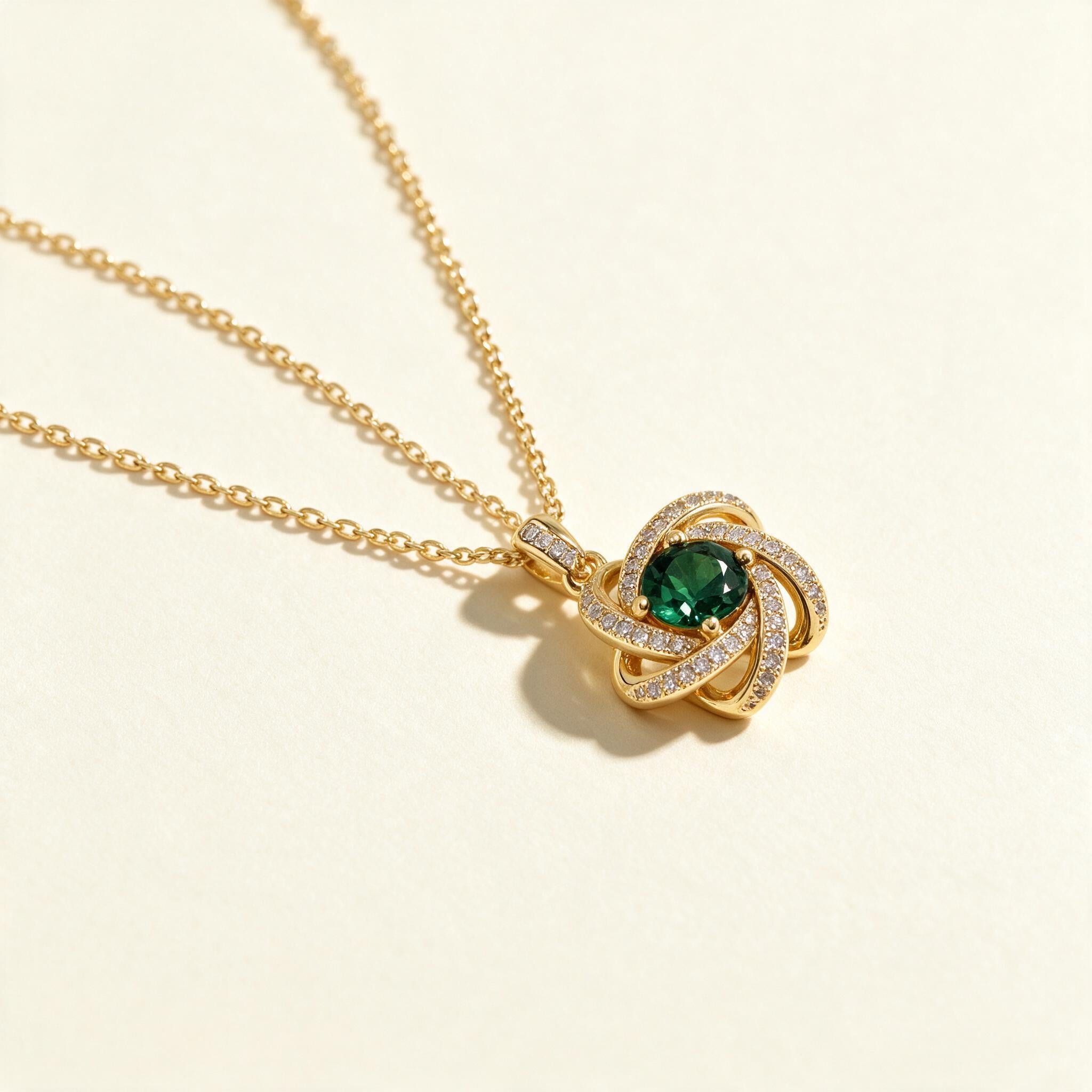 Gold-tone cable chain necklace with a pave love knot pendant set with a round green stone