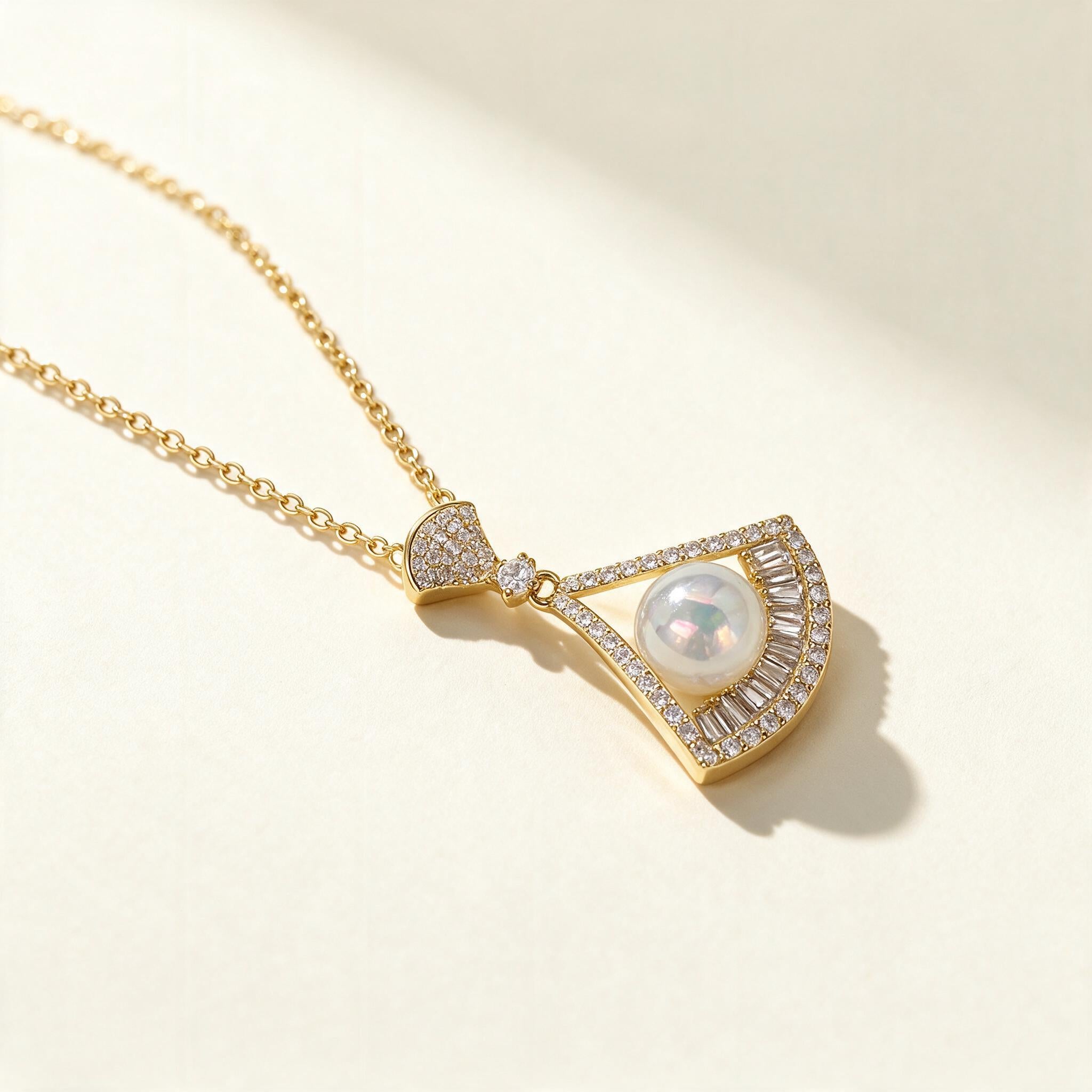 Gold-tone fan pendant necklace with a white shell pearl framed by baguette crystals