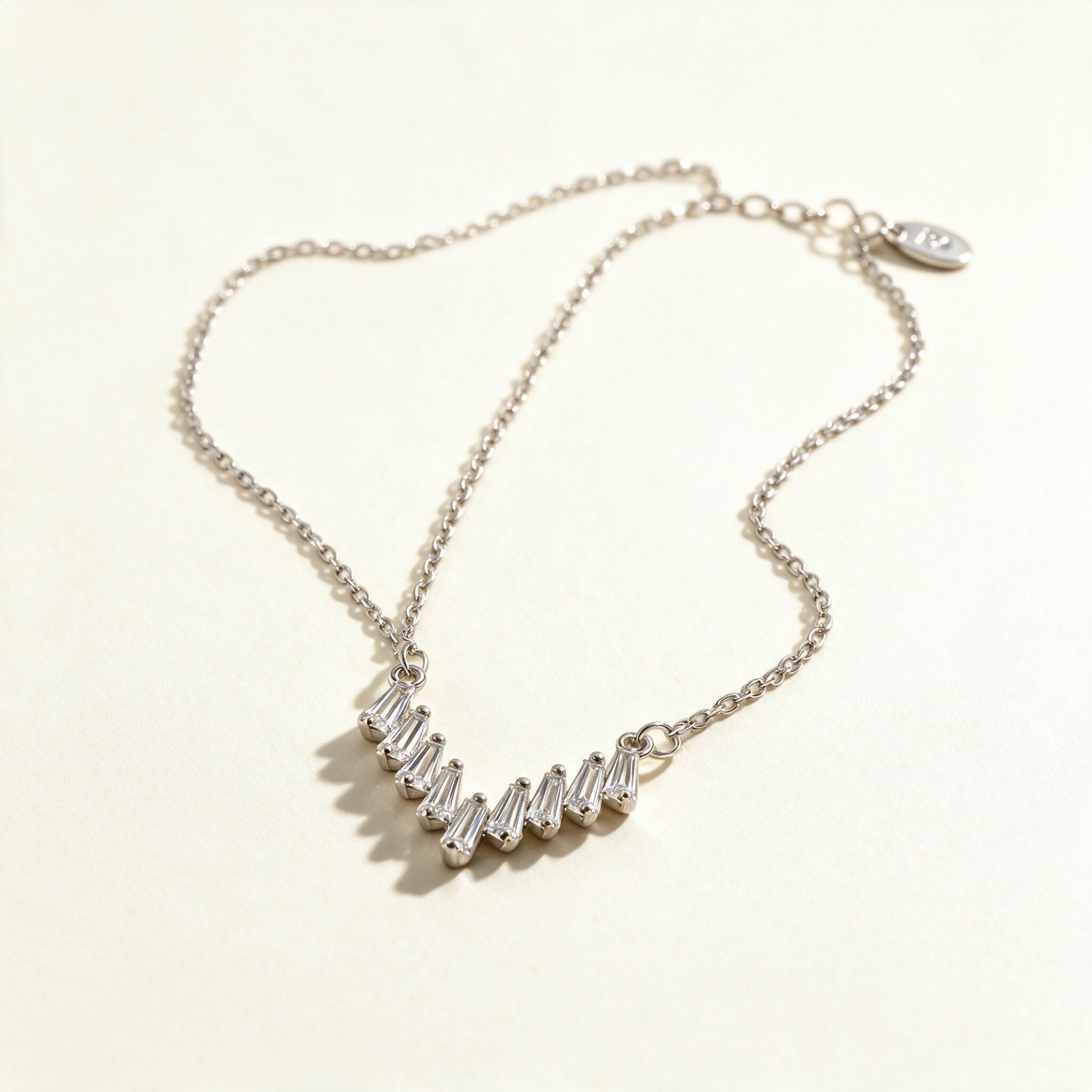 Silver-tone fine chain necklace with a curved fan of tapered baguette cubic zirconia stones on ivory background