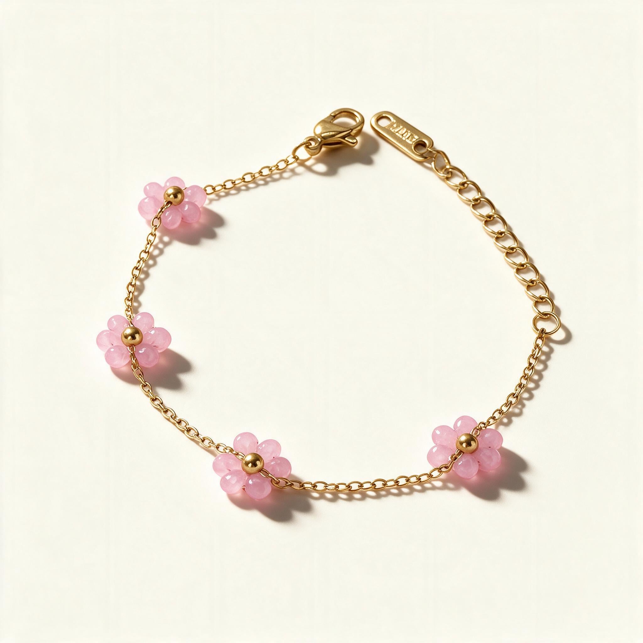 Gold-tone chain bracelet with pink frosted floral beads on ivory background