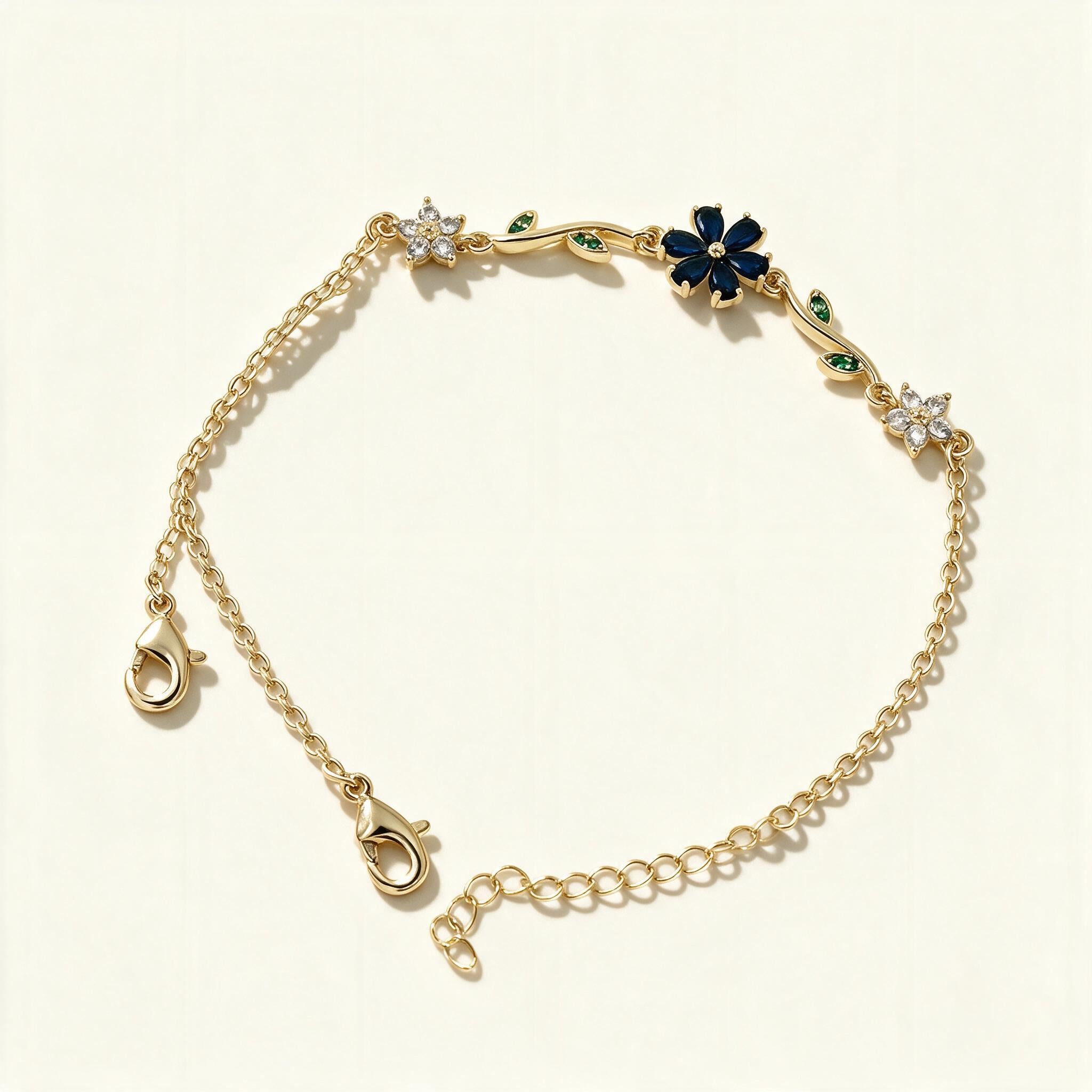 Gold-tone chain bracelet with navy blue enamel flower and green leaf accents