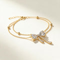 Gold-tone double chain bracelet with heart cubic zirconia bow charm and bead stations on ivory background