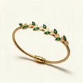 Gold-tone cable bangle with gold leaves and emerald green marquise stones