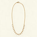 Gold-tone chain necklace with hanging cubic zirconia drops on ivory background