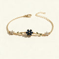 Gold-tone chain bracelet with navy blue flower, green leaf vines and clear crystal flowers on ivory background