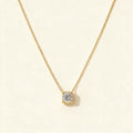 Gold-tone single fine chain necklace with a round cubic zirconia solitaire slider pendant on ivory background