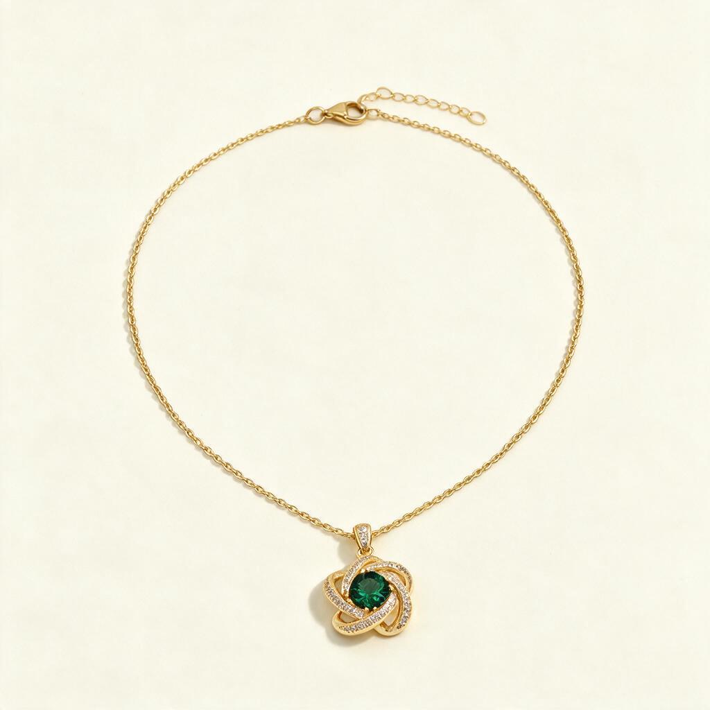 Gold-tone single chain necklace with emerald green knot pendant on ivory background