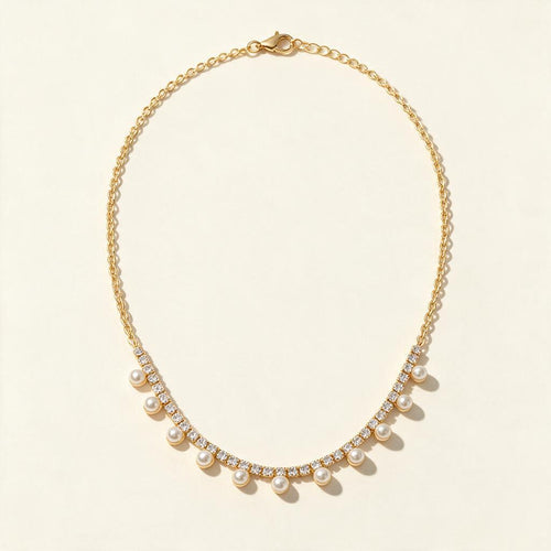 Gold-tone necklace with crystal tennis section and hanging pearl drops on ivory background