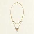 Gold-tone double chain necklace with a clear crystal bow and pavé ribbon tails on ivory background
