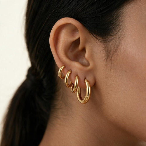 Woman wearing all three sizes of the huggie hoop set stacked in one ear